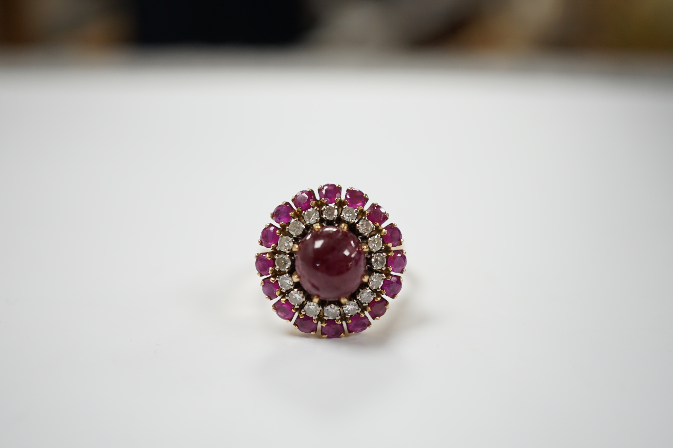 A yellow metal, ruby and diamond set circular cluster dress ring, with central cabochon ruby, size M/N, gross 8.2 grams.